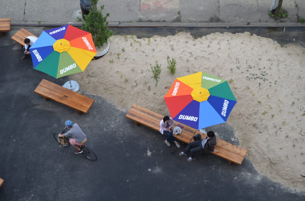 DUMBO Projects and Public Art: The Archive - Dumbo Beach Umbrellas with people sitting on the bench.
